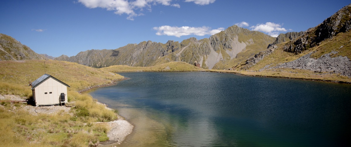 A backcountry hut sits next to a high country lake in summer
